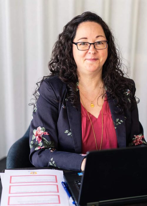 Tina i blomstret jakke ved pc med redskabspapirer på bordet ved siden af
